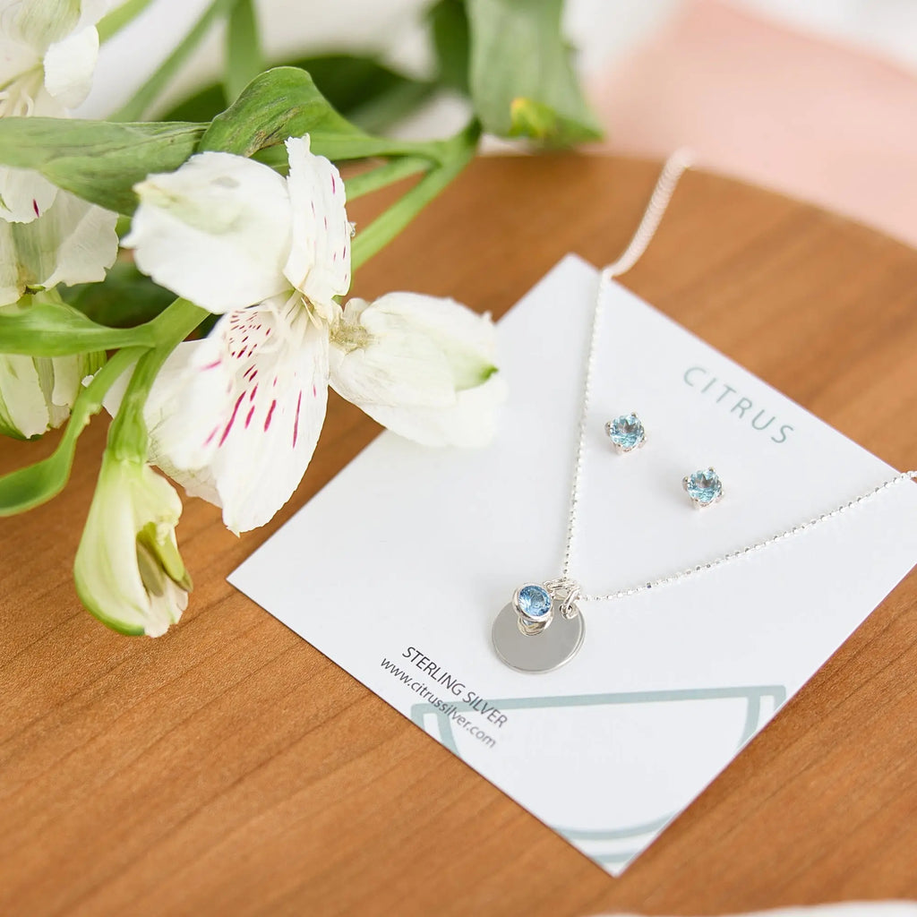Jewelry set with necklace and earrings on a card, surrounded by flowers on a wooden surface