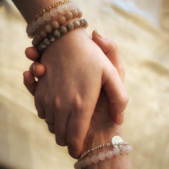 Two hands holding each other with beaded bracelets on a soft background