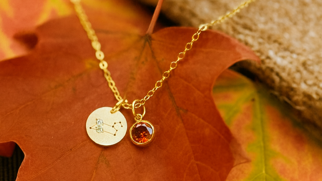 Gold necklace with a round pendant and a small round gemstone on autumn leaves.
