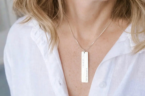 Woman wearing a sterling silver necklace with a rectangular pendant that show GPS Coordinates by CITRUS.
