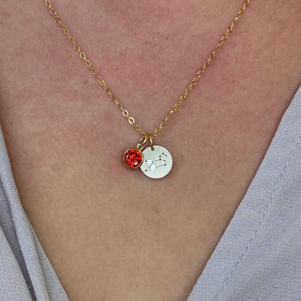 Gold necklace with a silver and red pendant on a person's arm.