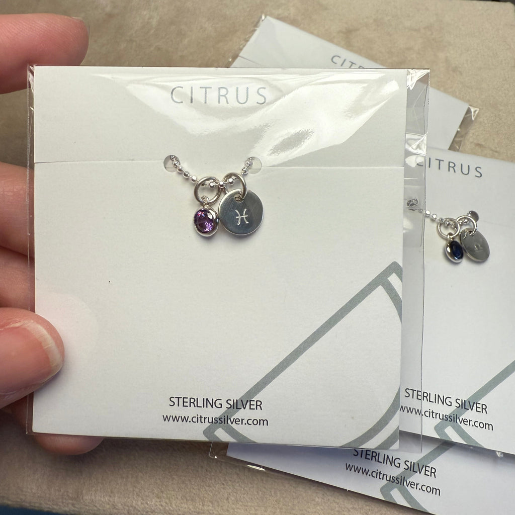 Silver earrings with a purple gemstone on a Citrus Sterling Silver card.