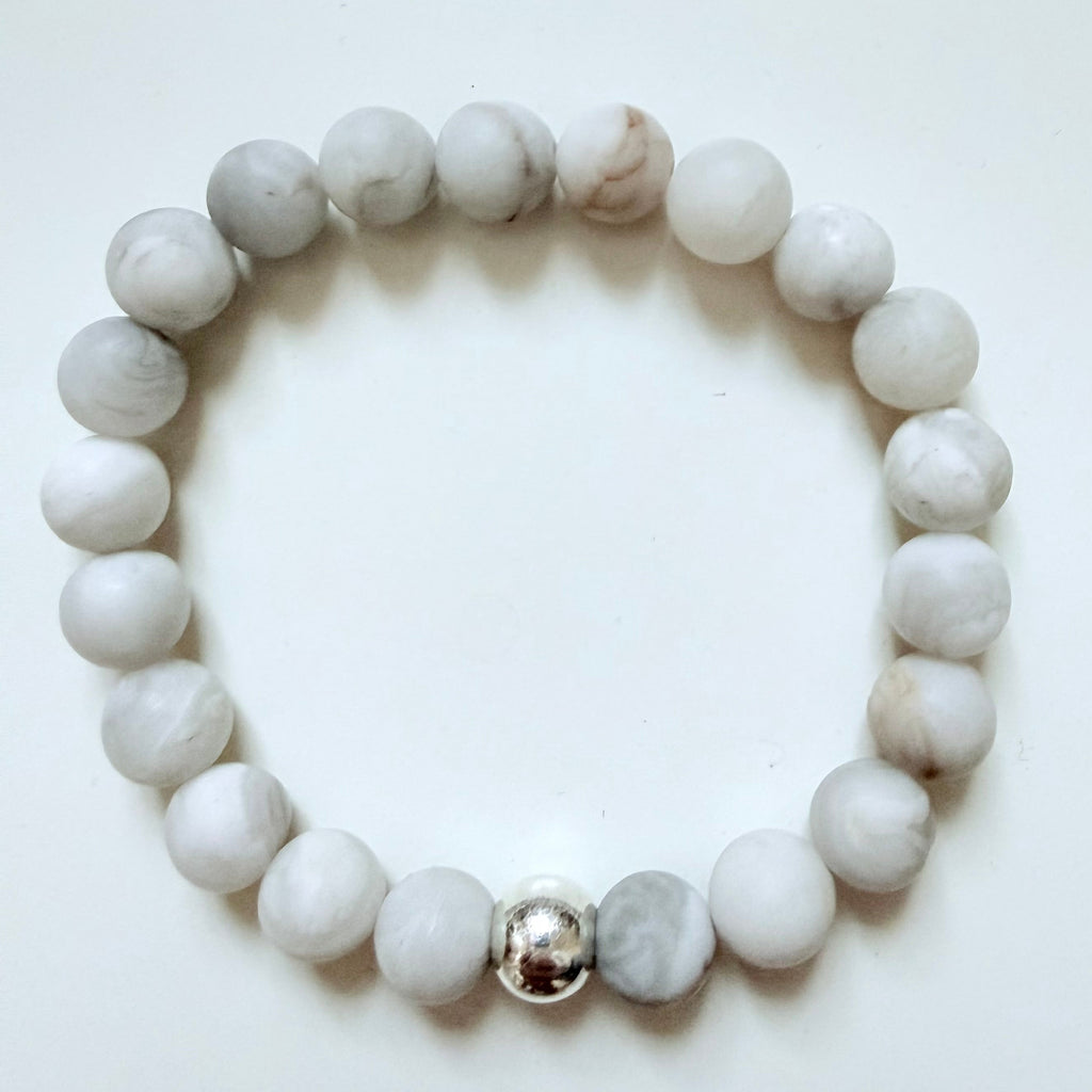 White beaded bracelet with a silver charm on a white background