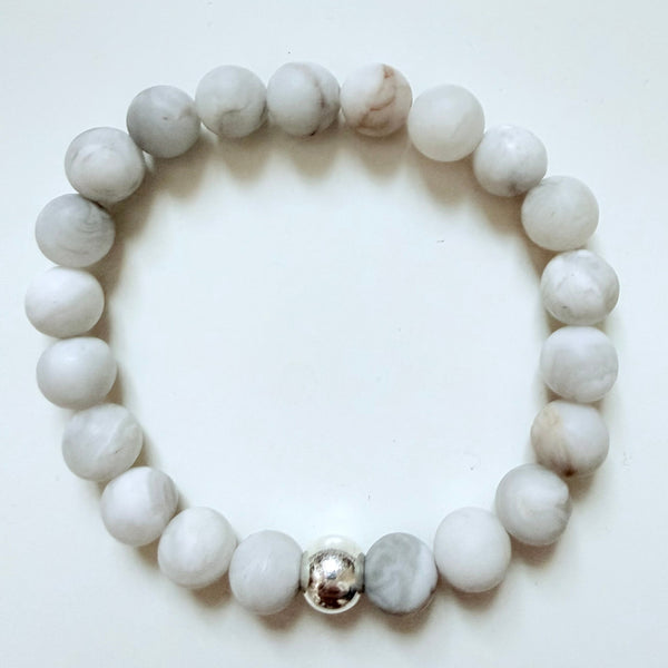 White beaded bracelet with a silver charm on a white background