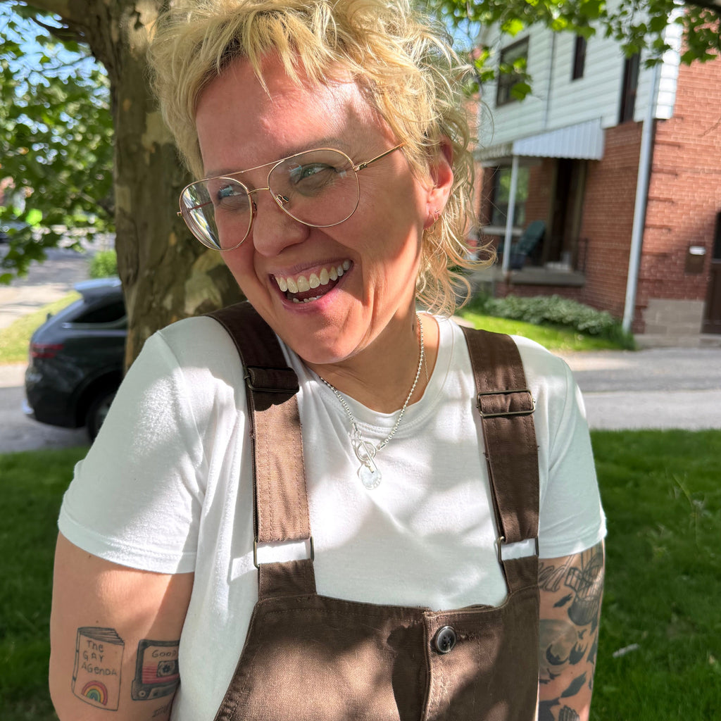 Person wearing love necklace with silver chain hand stamped with QUEER