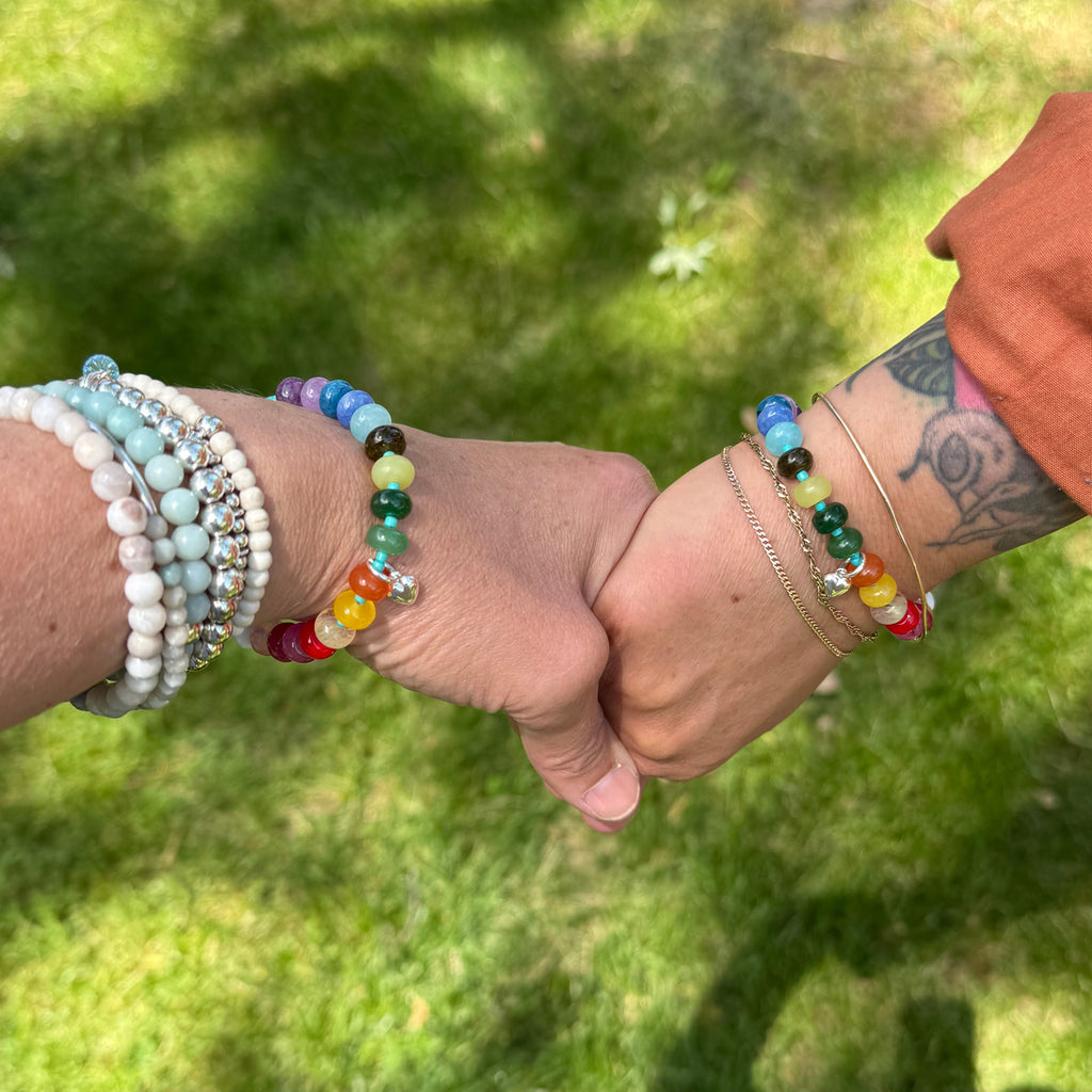 Two hands holding each other with colorful bracelets on a grassy background
